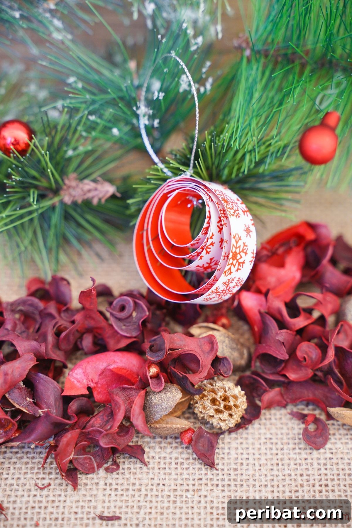 Layered Rolled Paper Christmas Charm 17 red and white paper ornament hanging on tree in front of red potpouri