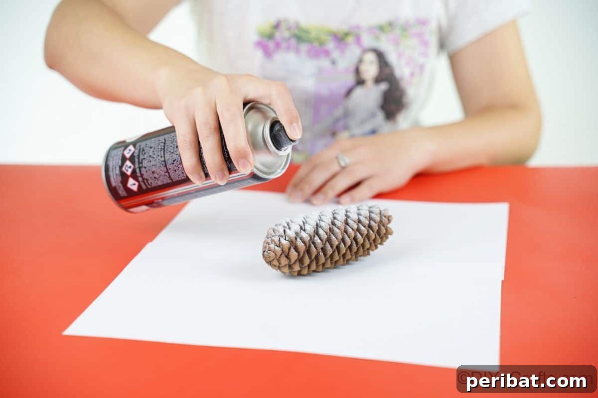 Winter Pinecone Penguin Fun 11 A hand gently spraying white paint onto a pinecone, creating a delicate frosted effect for the penguin's body.