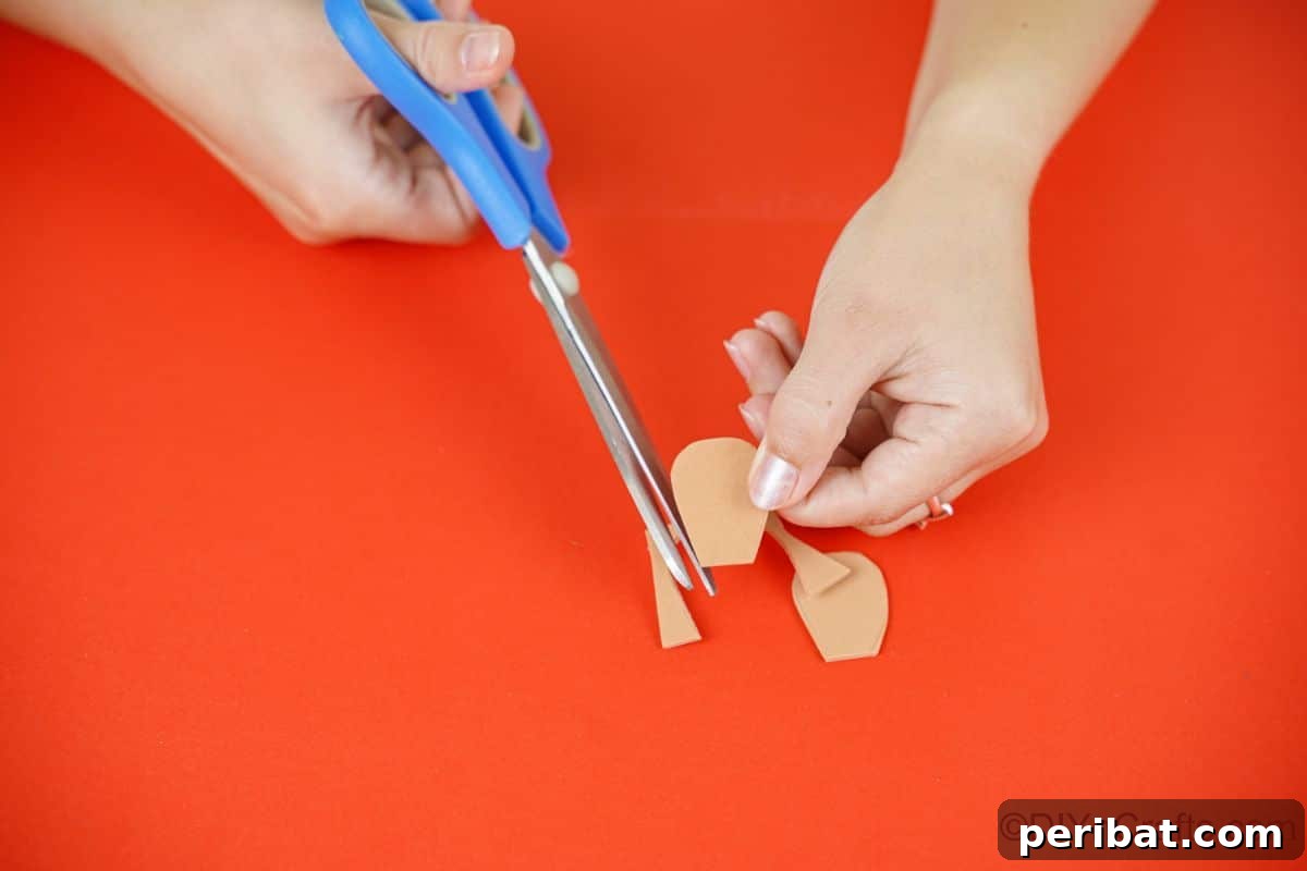Winter Pinecone Penguin Fun 14 Blue scissors precisely cutting a webbed foot shape out of brown foam paper, creating the penguin's feet.
