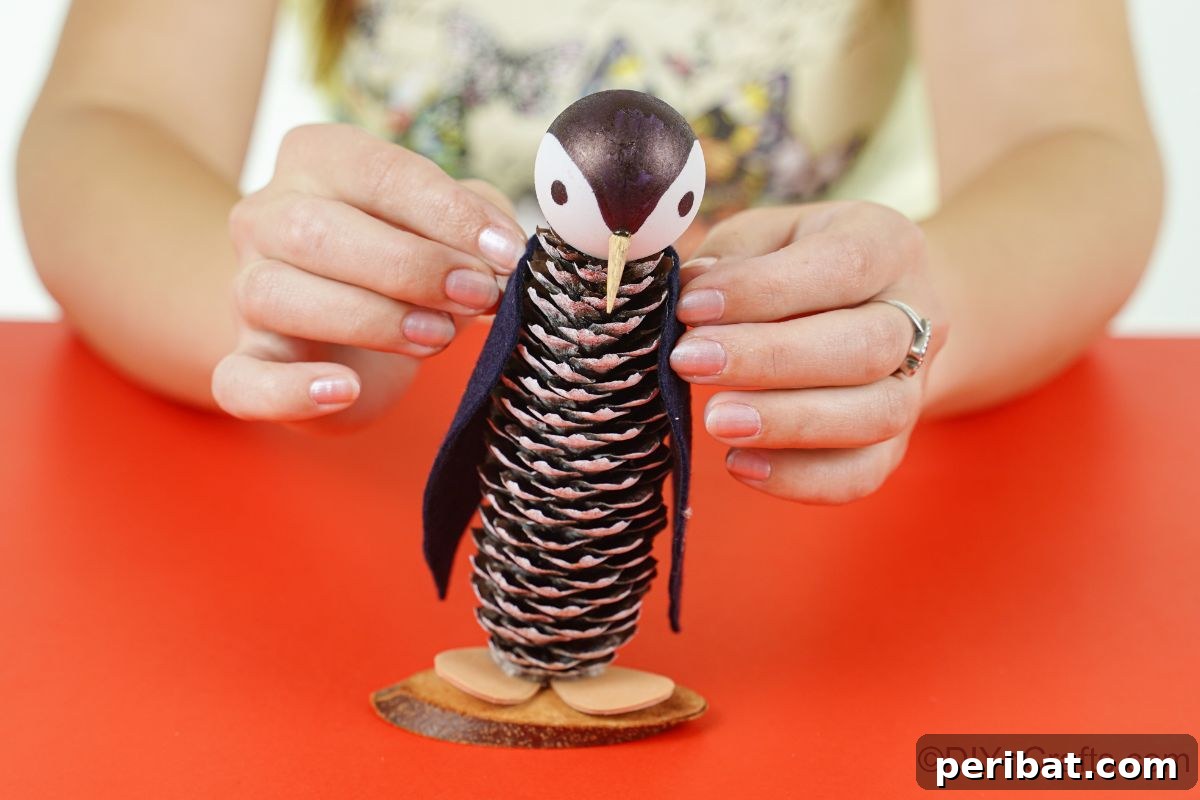 Winter Pinecone Penguin Fun 18 A person carefully gluing black felt wings onto the sides of the pinecone penguin's body, giving it its iconic silhouette.