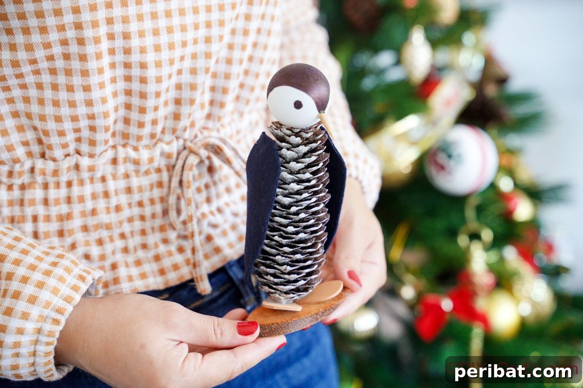 Winter Pinecone Penguin Fun 3 A person gently holding a finished pinecone penguin in front of a warm, twinkling Christmas tree, highlighting its rustic holiday charm.
