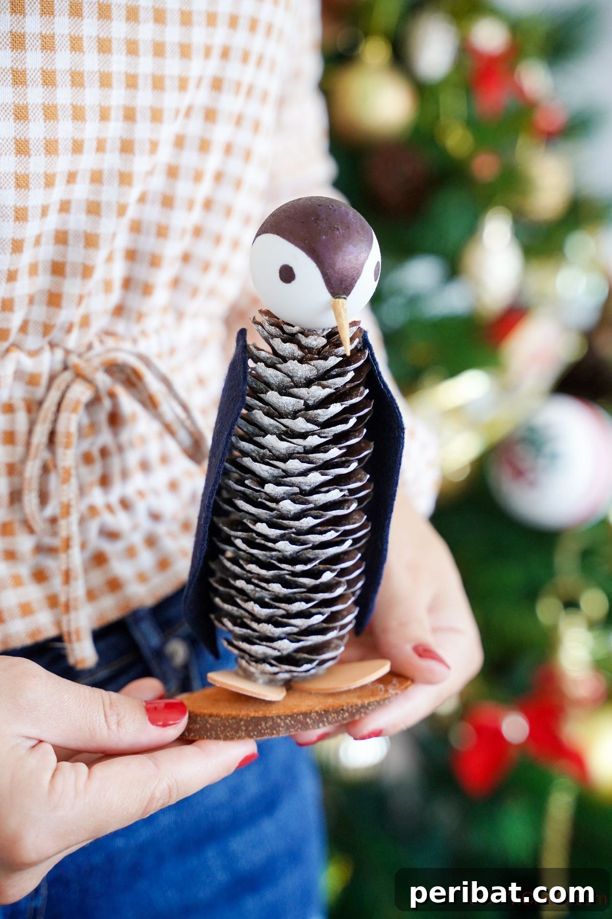 Winter Pinecone Penguin Fun 25 A woman in a cozy checked shirt proudly holding a finished pinecone penguin craft, showcasing its delightful details.