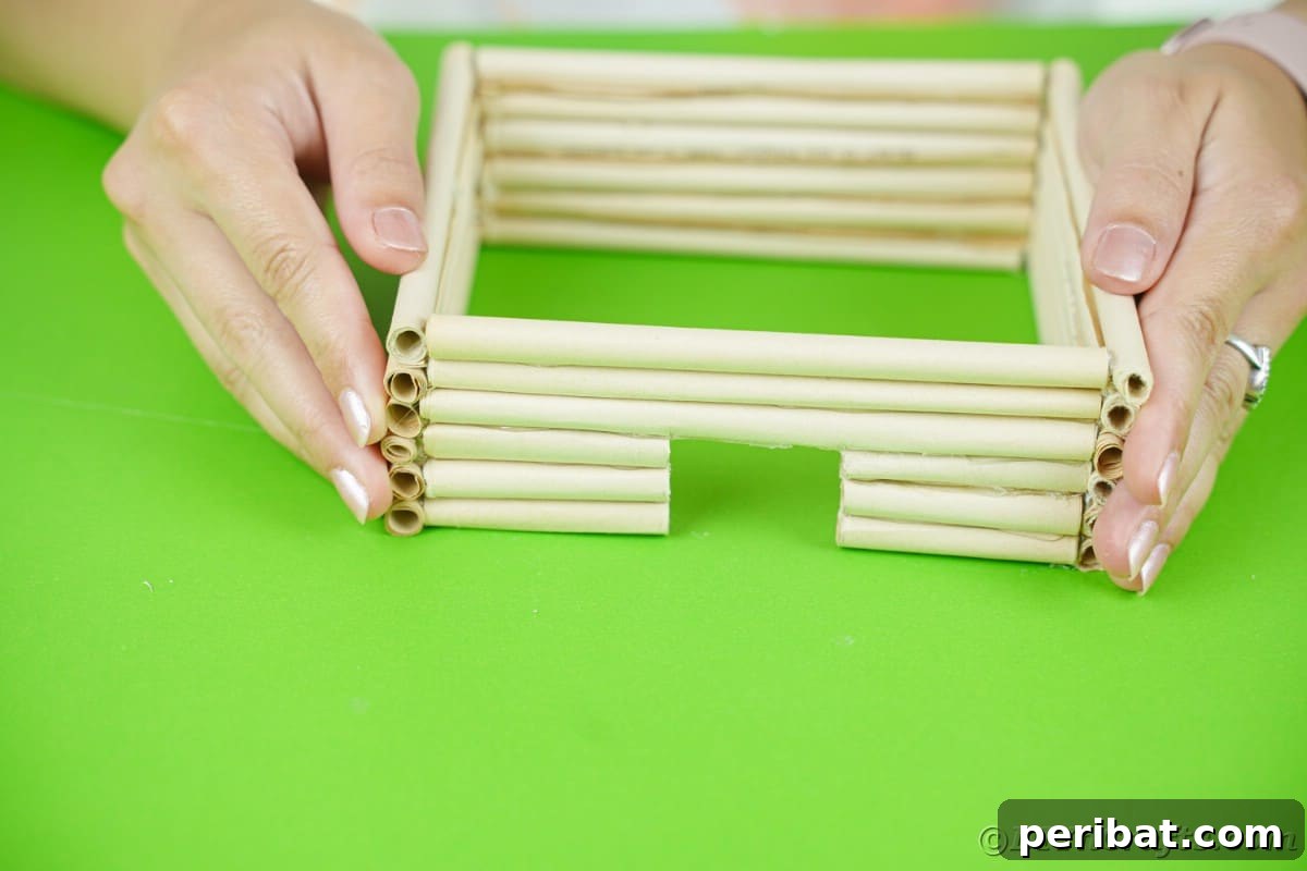 paper log house base being held by hands on green table