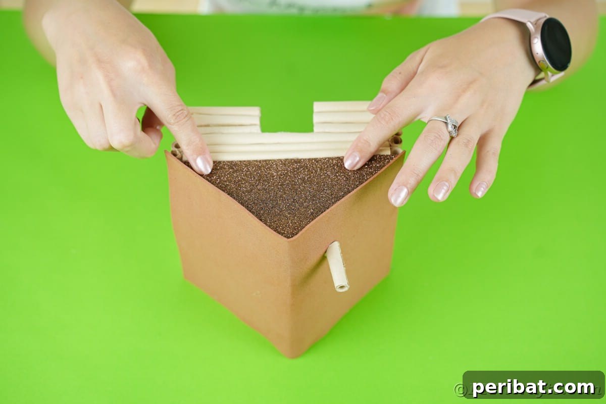gluing brown glitter paper to the ends of a miniature log cabin