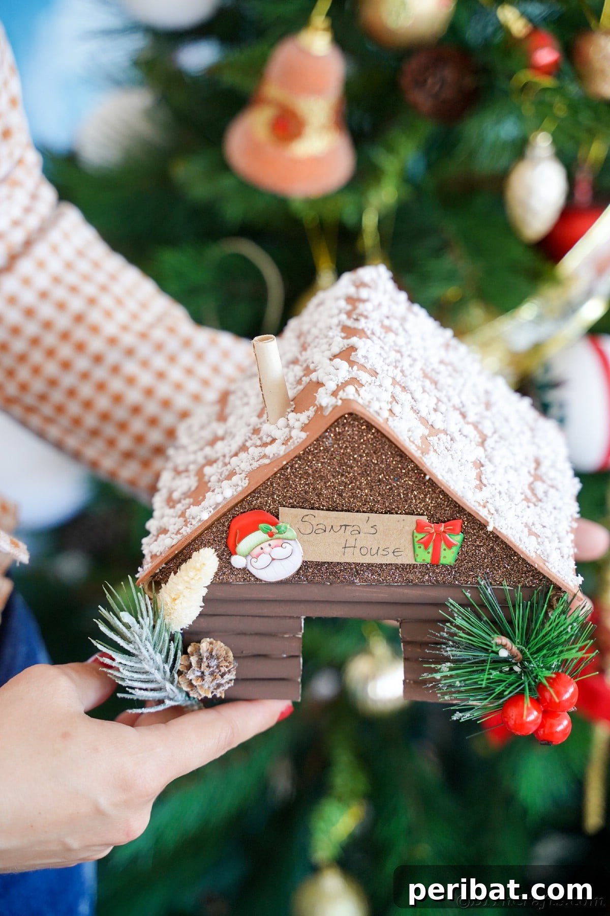 lady holding miniature rustic log santas workshop in front of tree