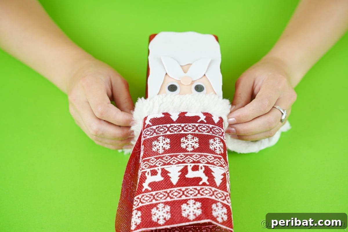 Jolly Upcycled Milk Carton Santa Candy Box 16 Hands wrapping a strip of white fake fur around the base of the hat on the box