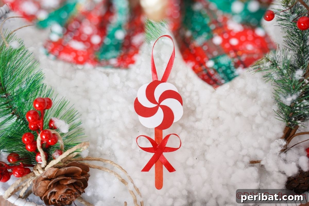 Sweet Peppermint Stick Decor 4 Paper peppermint candy ornament resting on fake snow, emphasizing its winter holiday theme.