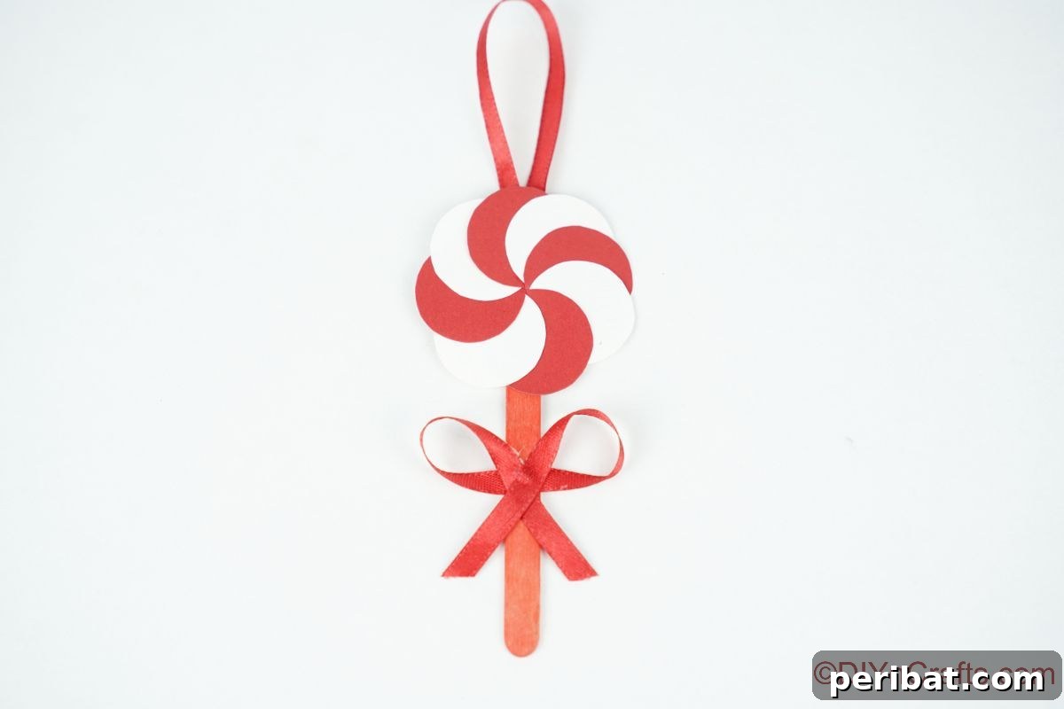 Sweet Peppermint Stick Decor 5 Paper peppermint candy ornament on a white table, showcasing its simple yet elegant design.