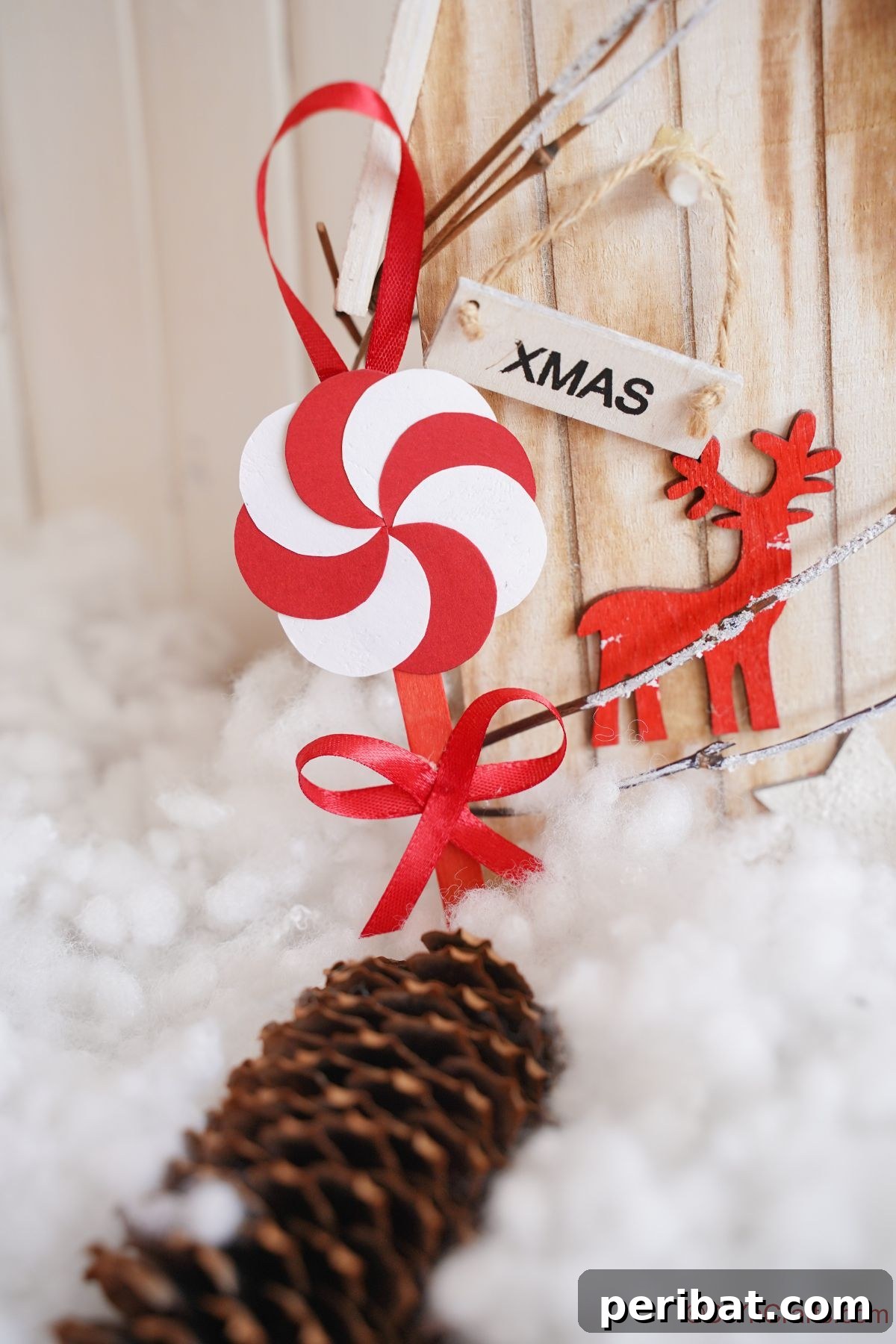 Sweet Peppermint Stick Decor 6 Paper peppermint candy ornament hanging on a wooden surface next to a red wooden reindeer, highlighting festive decor.