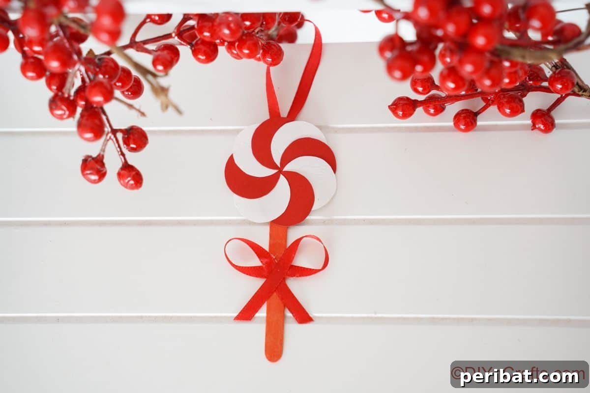 Sweet Peppermint Stick Decor 8 Peppermint candy ornament hanging against a white wall with fake berries, illustrating a delightful festive accent.