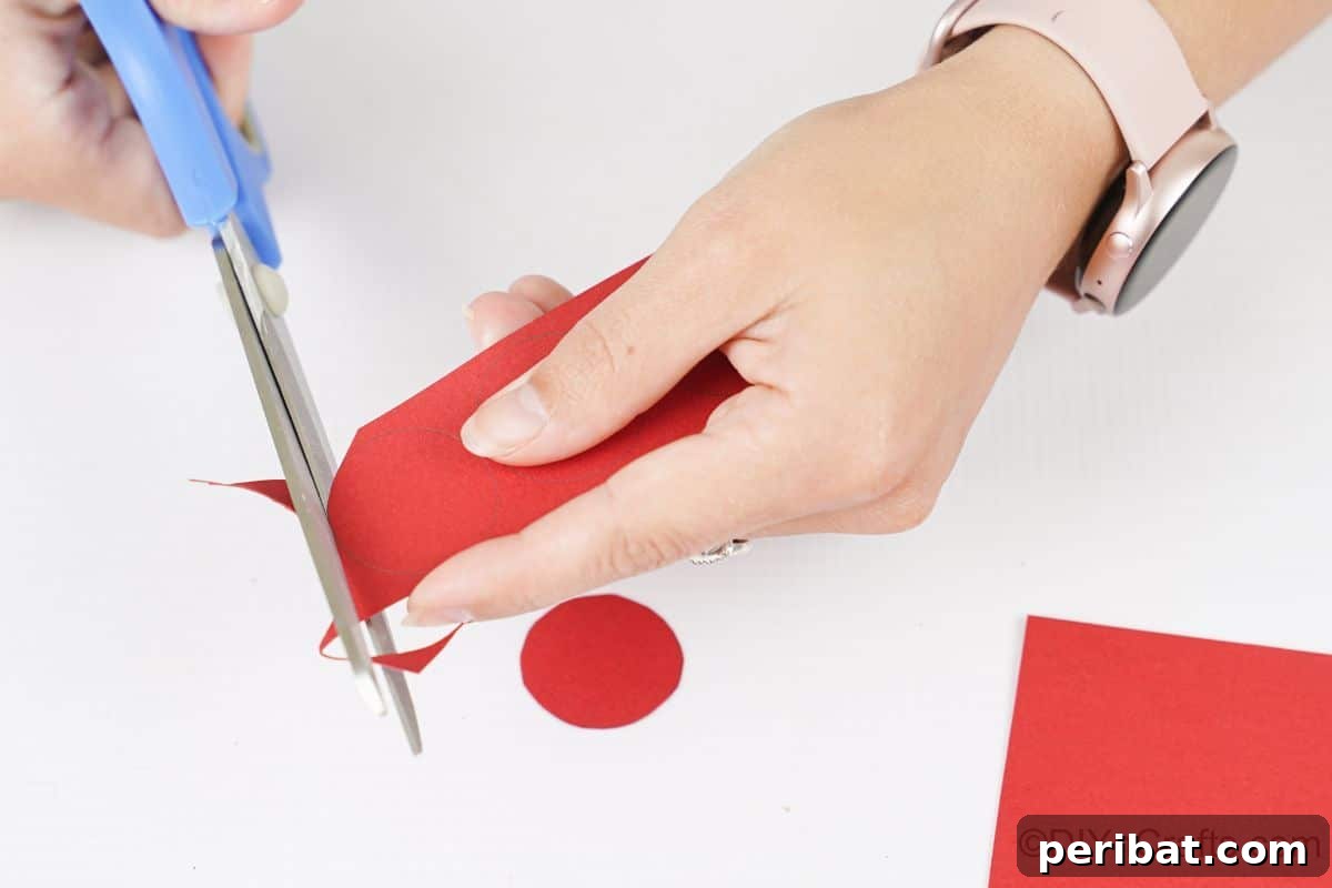 Sweet Peppermint Stick Decor 10 Hand holding blue scissors cutting circles from red paper, showing the initial step of preparing materials.