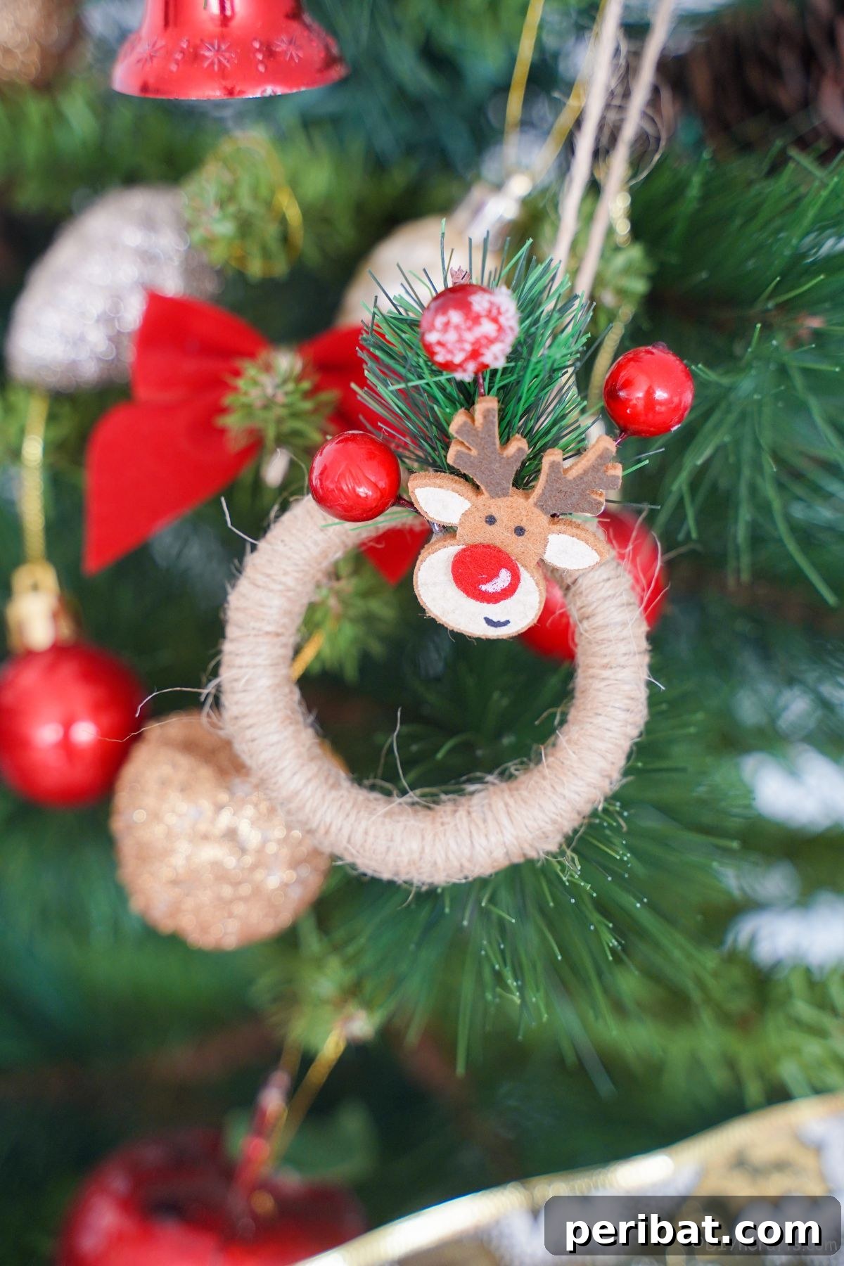 Twine-wrapped mini wreath with a Rudolph figurine and berries, hanging on a beautifully decorated Christmas tree, evoking rustic holiday charm.