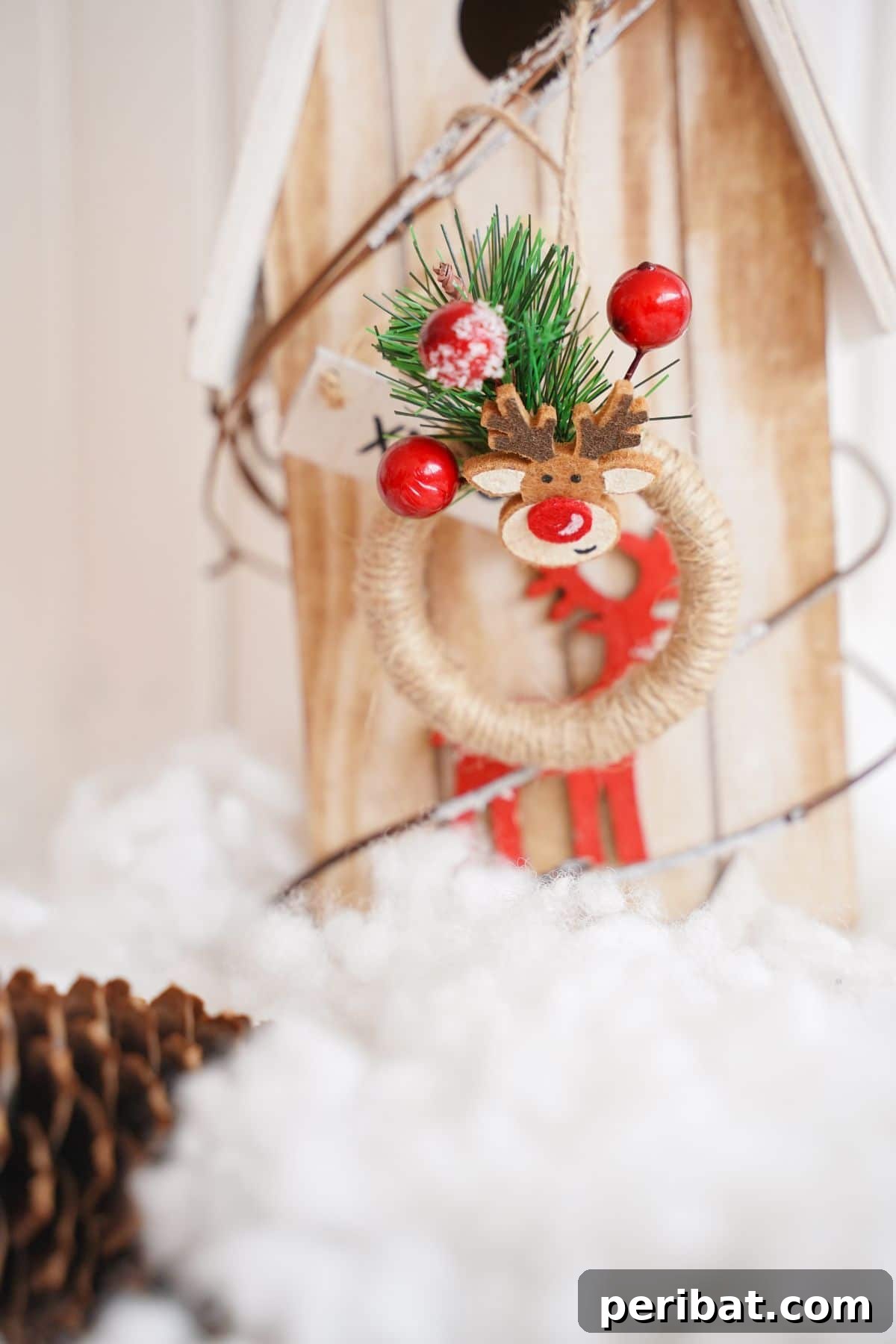 A rustic miniature wreath ornament, beautifully crafted, displayed on a small wooden birdhouse amidst fake snow, suggesting cozy winter decor ideas.