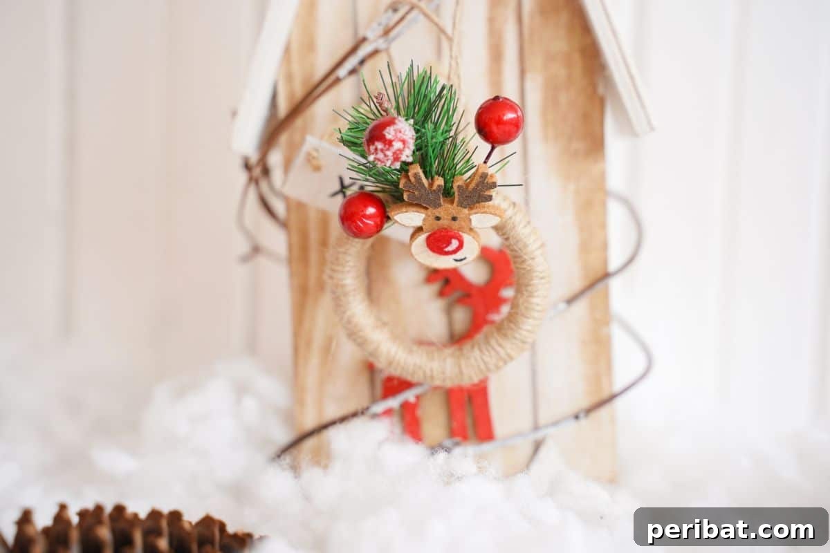 A rustic mini wreath ornament, adorned with festive details, hangs on the front of a charming wooden birdhouse placed on fake snow, suggesting versatile decor placements.