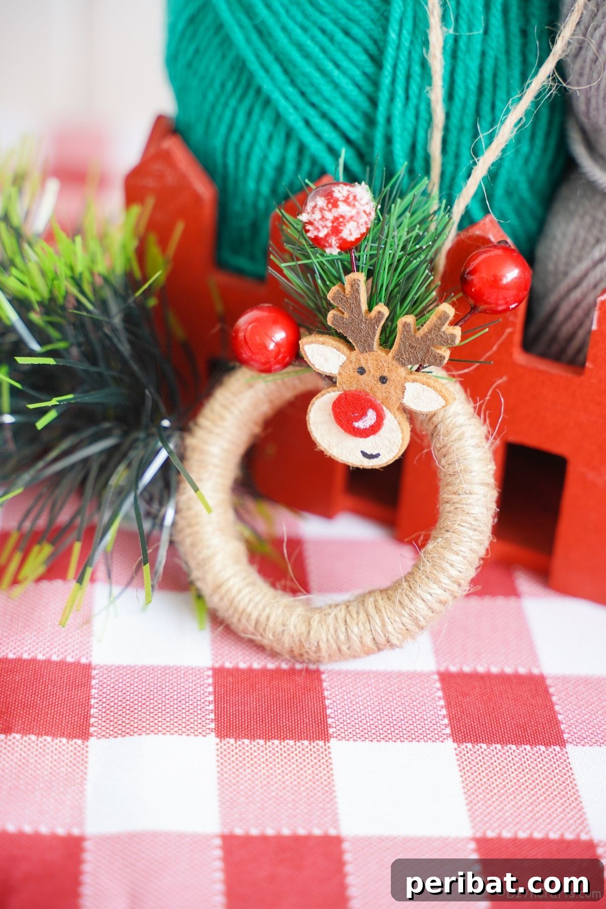 A finished miniature wreath ornament, showcasing its rustic twine wrapping and festive accents, rests against a red basket on a classic checked tablecloth, ready for display.