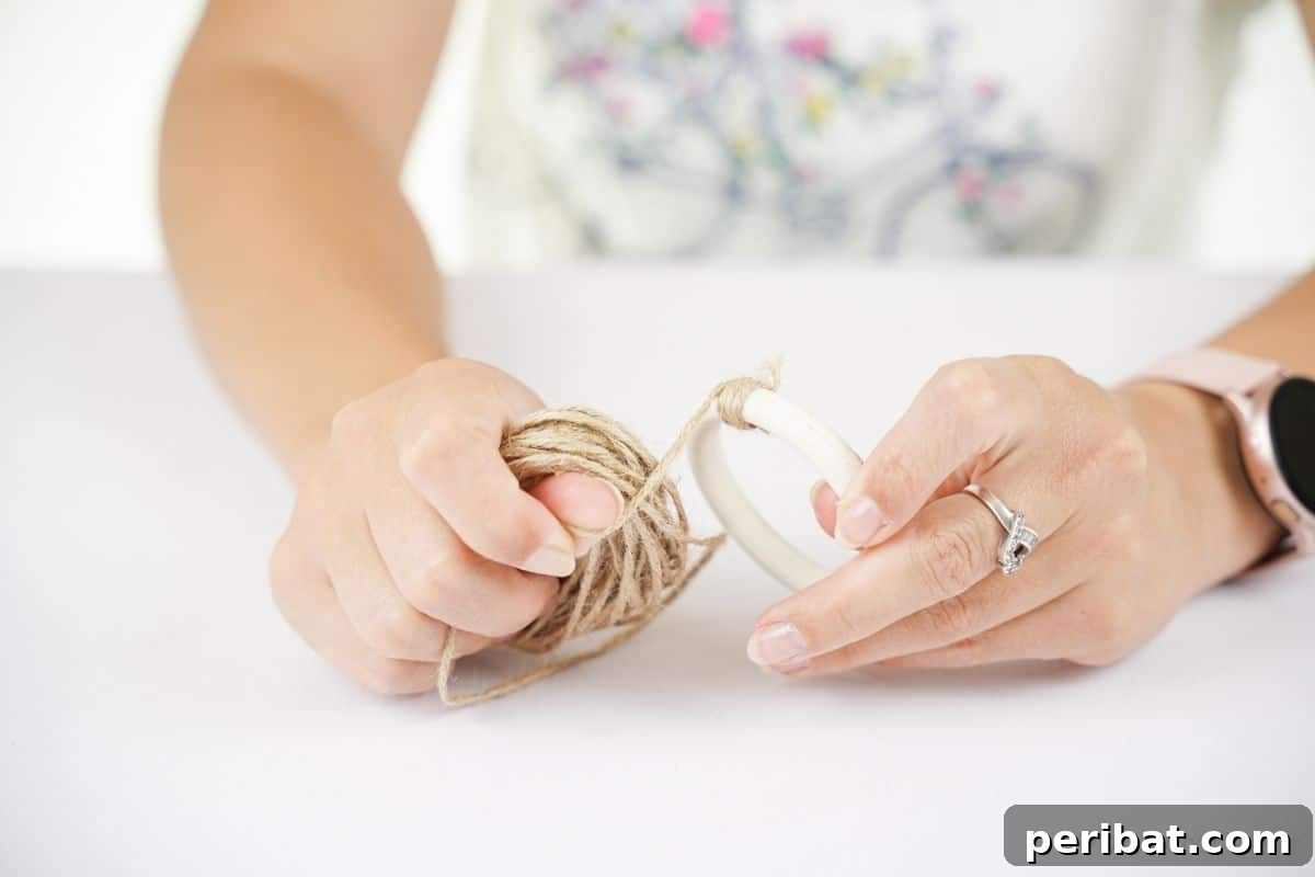A person demonstrates securing twine to a Styrofoam ring, showing the initial wrapping step for the mini wreath ornament.