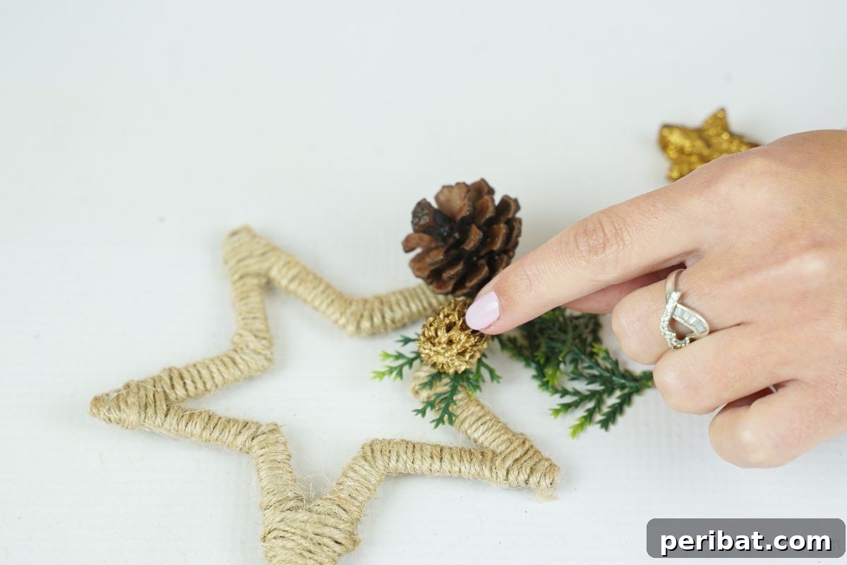 A finger gently holding a small pinecone onto the edge of a twine-wrapped star, adding a natural detail.
