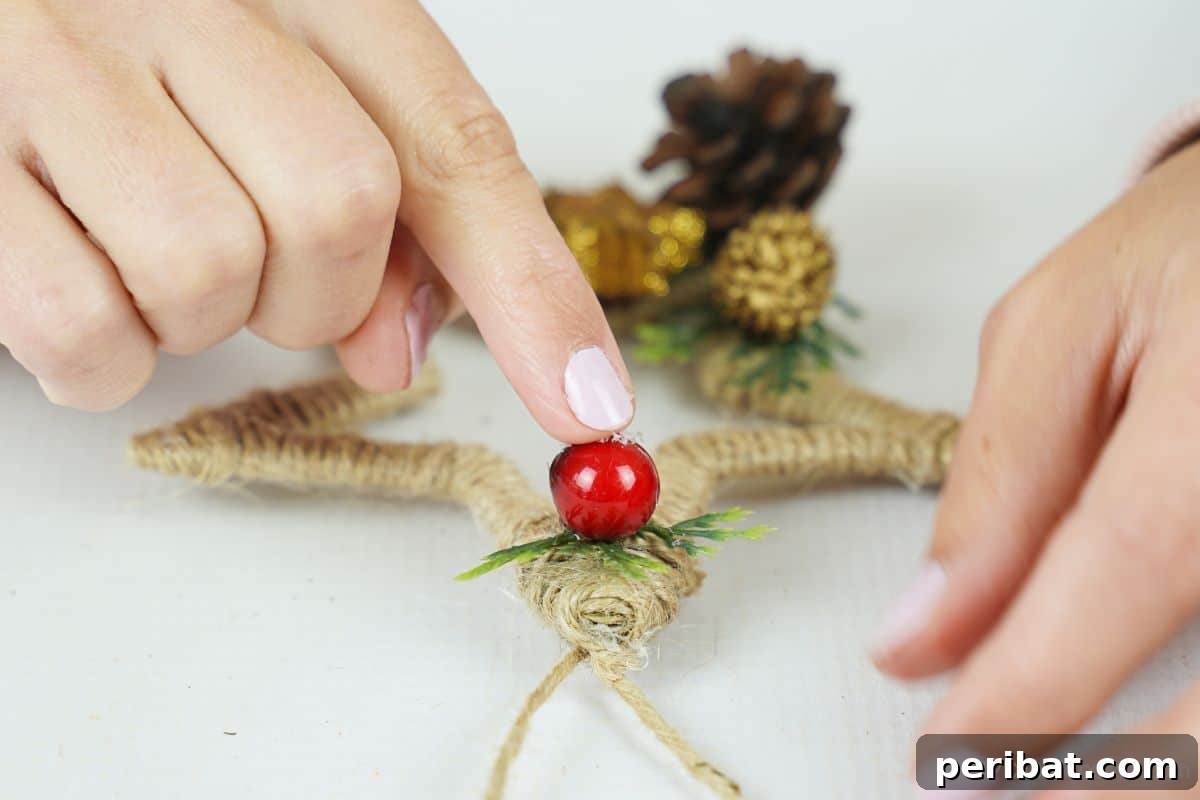 A finger gently positioning a bead on top of a finished twine-wrapped star, adding a decorative element.