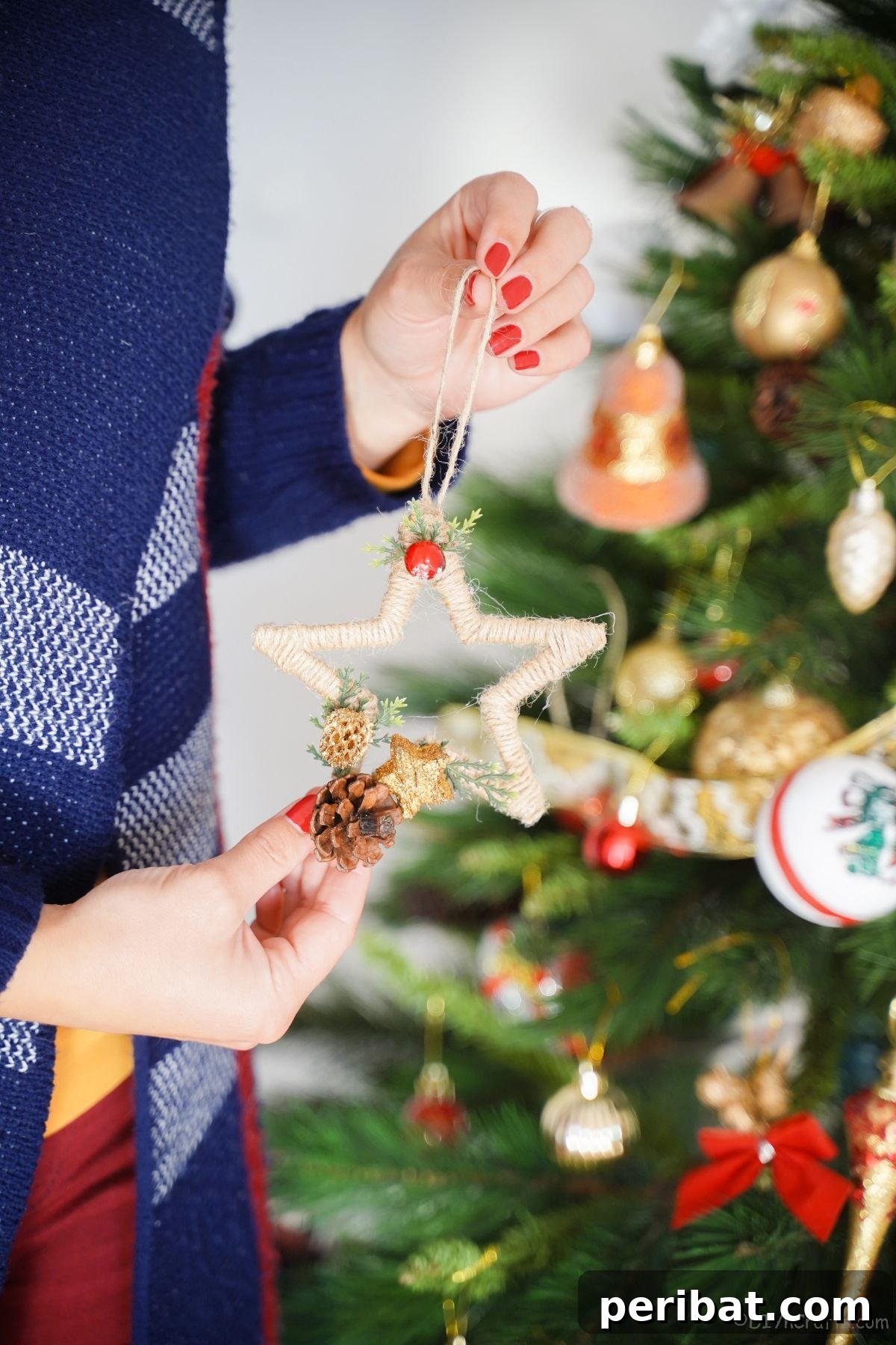 A rustic twine-wrapped star ornament held gently in front of a softly lit Christmas tree, ready to be hung.