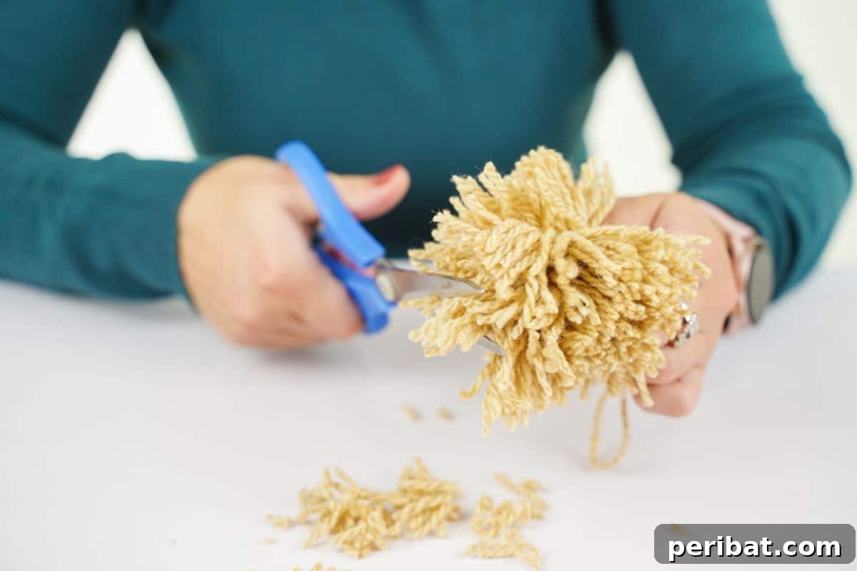 Festive Fluffy Reindeer Christmas Garland Craft 11 Blue scissors being used to trim excess yarn on a pom pom to make it rounder
