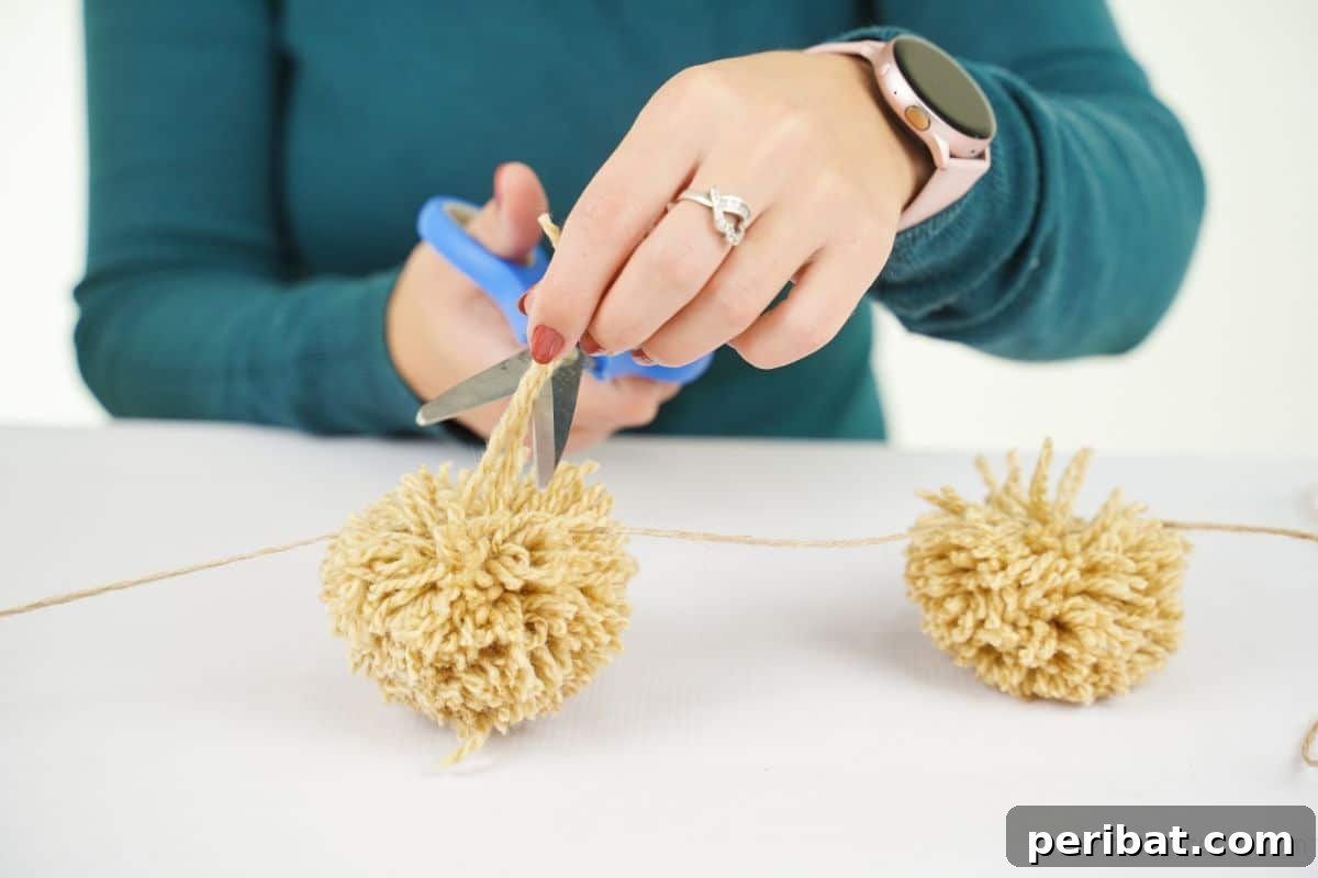 Festive Fluffy Reindeer Christmas Garland Craft 12 Blue scissors held, ready to cut yarn for attaching pom poms to the garland string