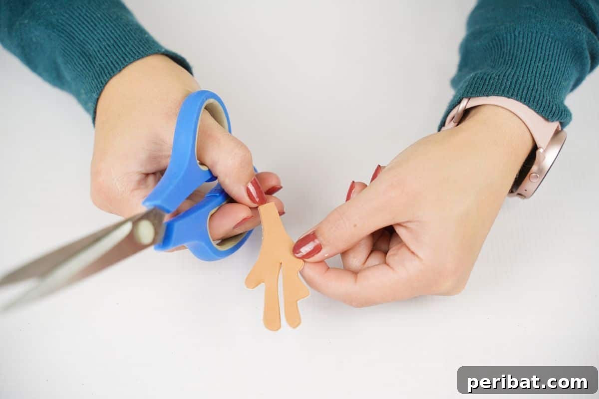Festive Fluffy Reindeer Christmas Garland Craft 13 A hand holding blue scissors and a brown paper antler cutout