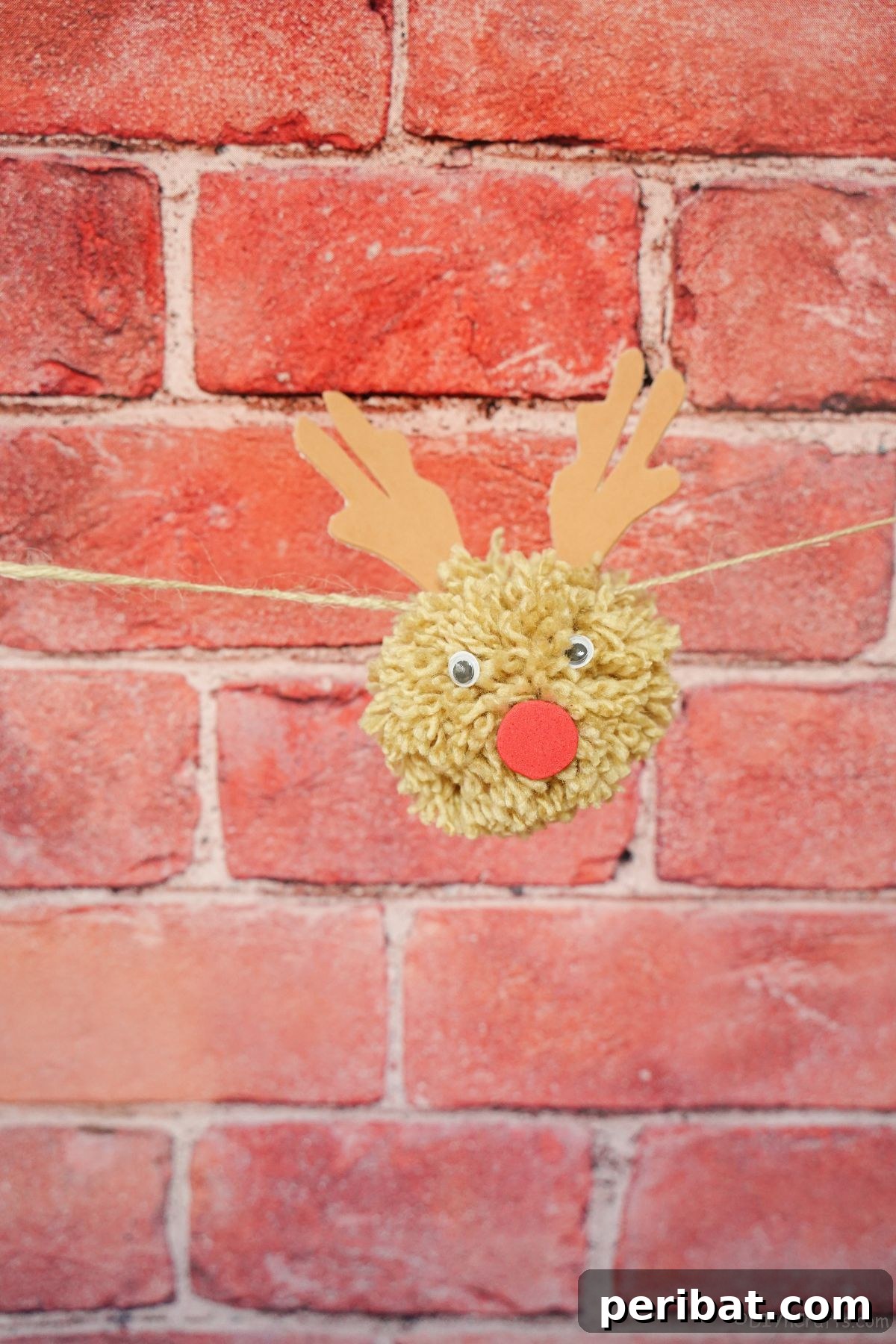 Festive Fluffy Reindeer Christmas Garland Craft 19 A single reindeer pom pom hanging against a rustic brick wall