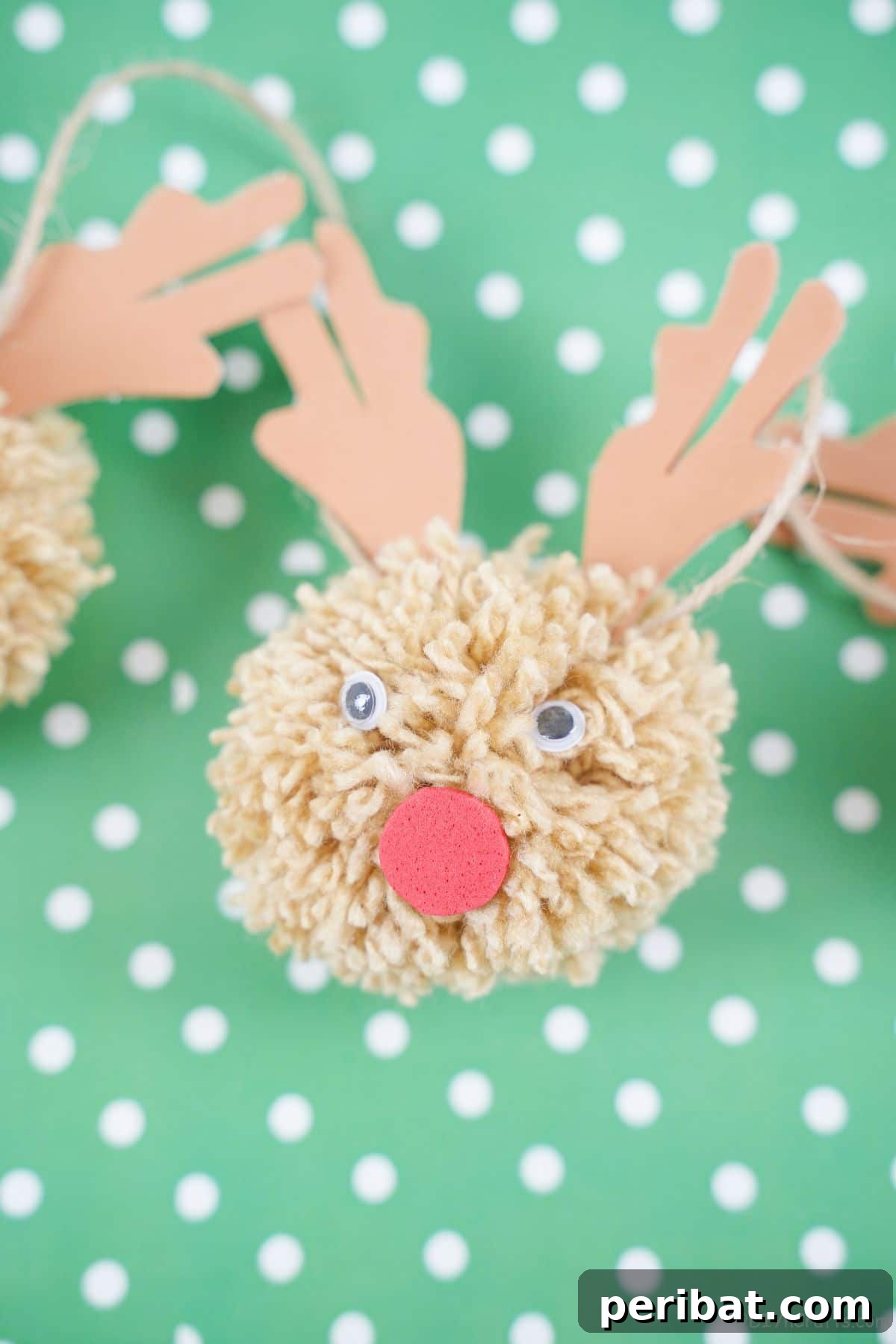 Festive Fluffy Reindeer Christmas Garland Craft 20 A yarn reindeer pom pom resting on green and white polka dot paper
