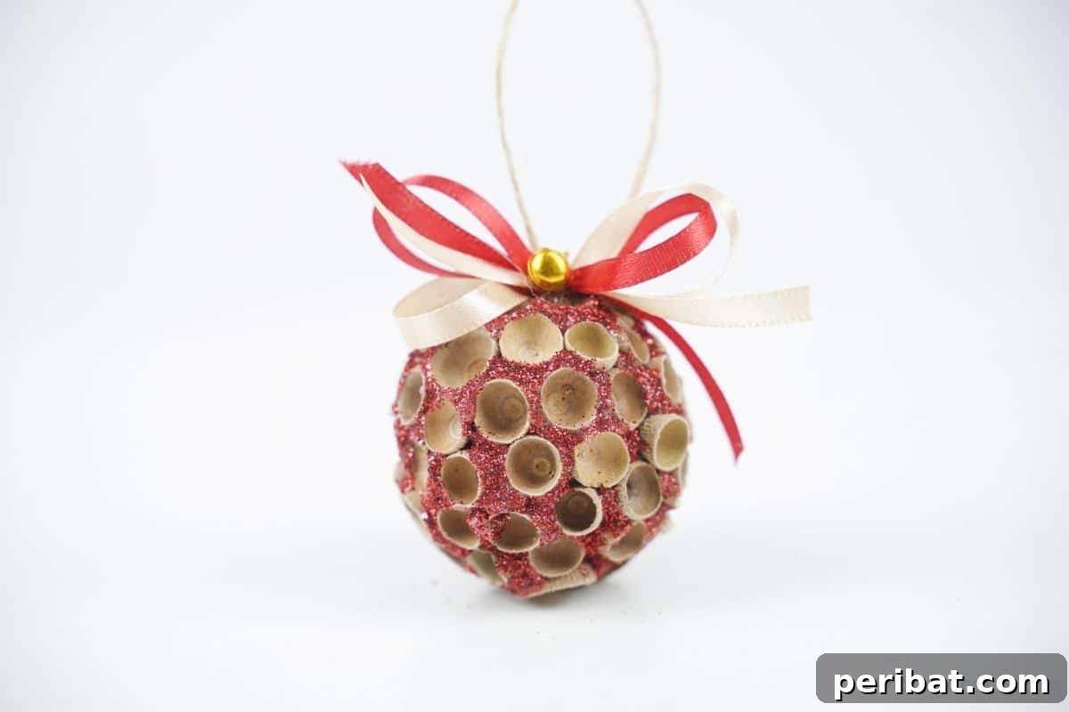 Handcrafted Sparkling Acorn Cap Christmas Ornament 7 A beautifully crafted glitter ornament with acorn caps, featuring shades of pink and red, sits on a pristine white table.