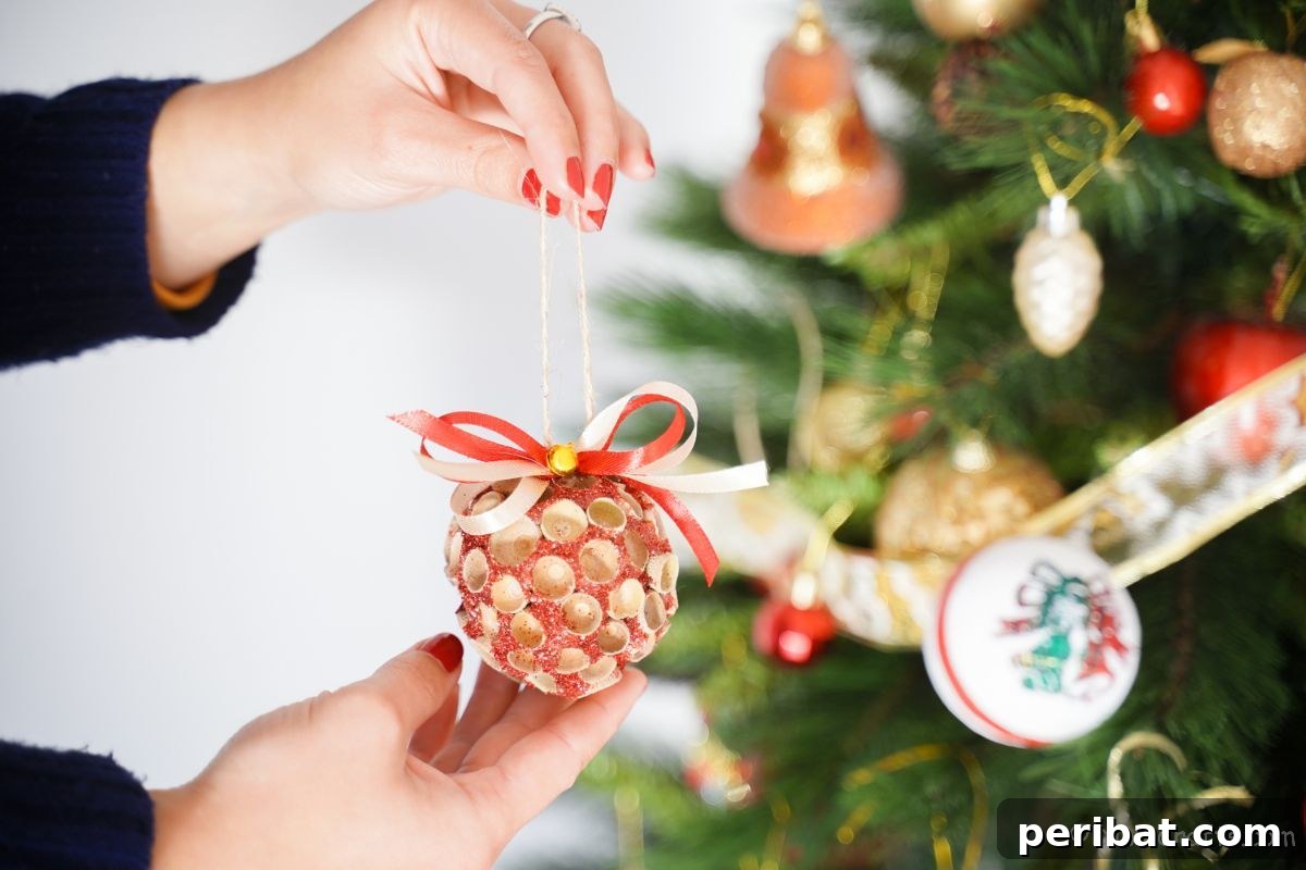 Handcrafted Sparkling Acorn Cap Christmas Ornament 8 A hand holds a completed glitter ornament with acorn caps, artfully positioned in front of a subtly blurred Christmas tree, highlighting its festive nature.