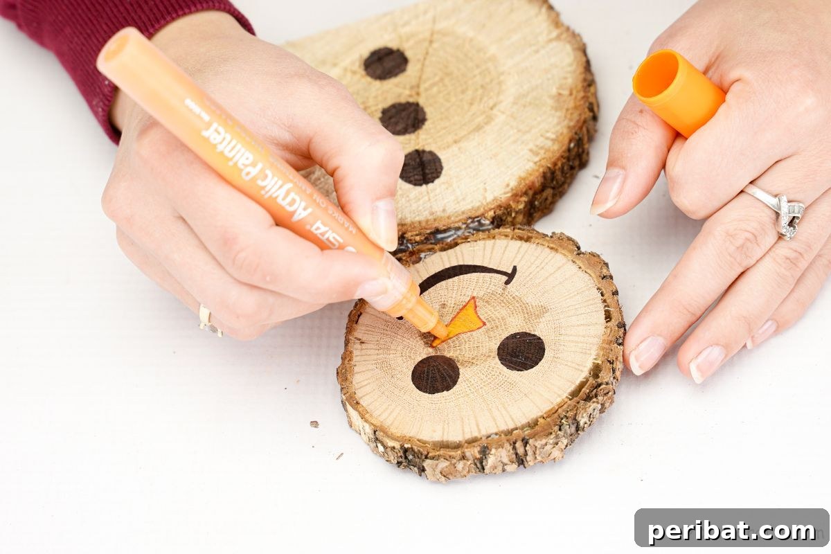 Charming Wood Slice Snowman Winter Display 12 A hand drawing a small, orange carrot-shaped nose onto the wood slice face of a snowman with an orange marker.