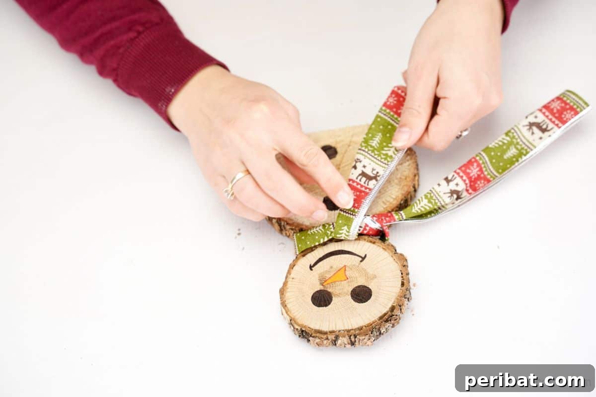 Charming Wood Slice Snowman Winter Display 13 Fingers adjusting a green holiday ribbon tied around the 'neck' of a wooden snowman, creating a scarf detail.