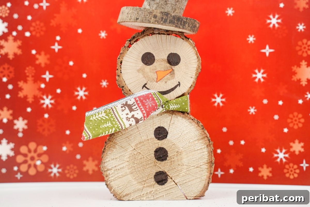 Charming Wood Slice Snowman Winter Display 3 Close-up of a wood slice snowman against a festive red background with white snowflakes, highlighting its green ribbon scarf and simple painted face.