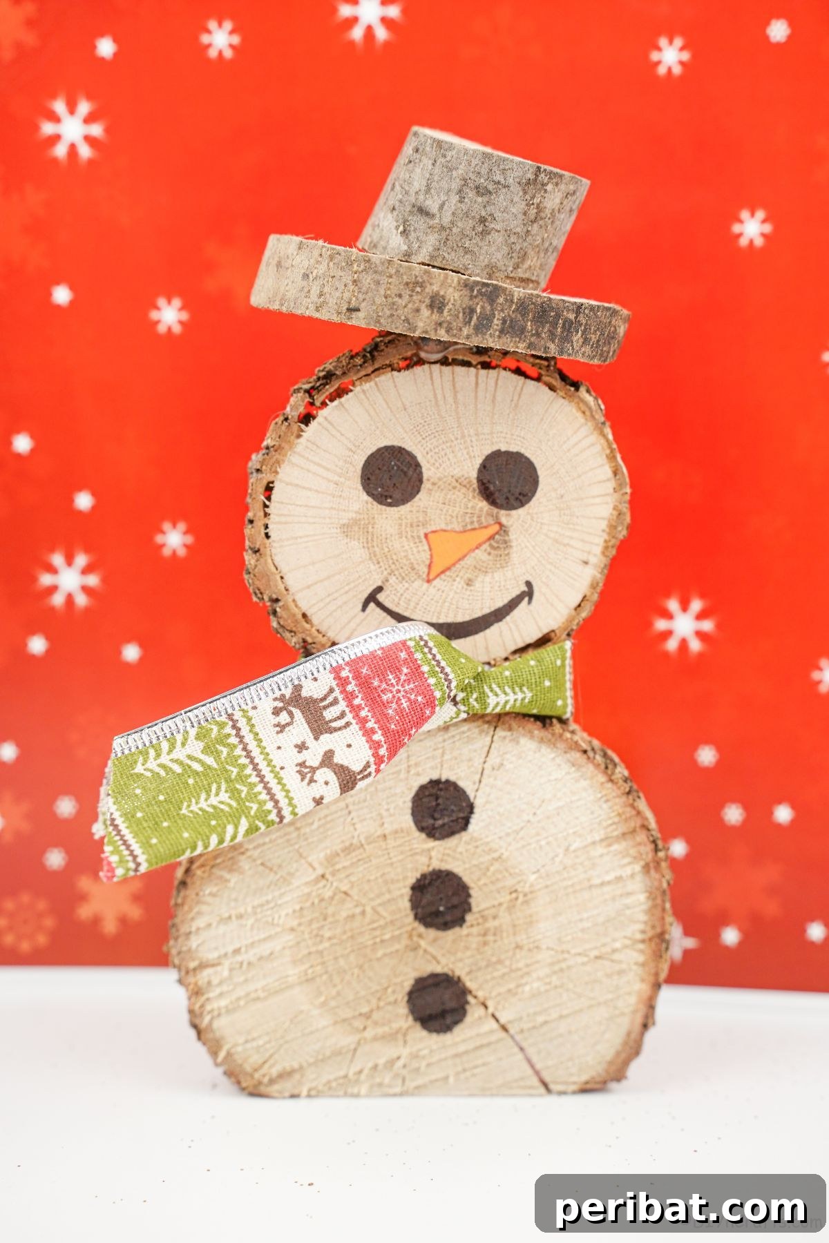 Charming Wood Slice Snowman Winter Display 17 A pair of charming wood slice snowmen, one larger and one smaller, with red scarves, displayed on a white table against a festive red background.
