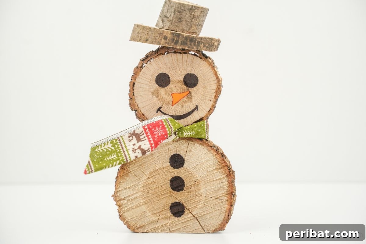 Charming Wood Slice Snowman Winter Display 6 A charming holiday wooden snowman, featuring a red and white checkered scarf, sitting on a white table next to a sprig of evergreen.