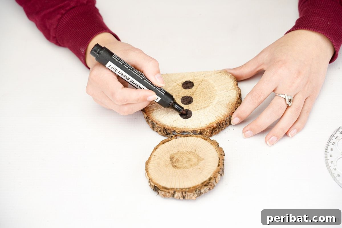 Charming Wood Slice Snowman Winter Display 10 A hand drawing three black circles on the lower wood slice of a snowman's body with a black marker, creating buttons.