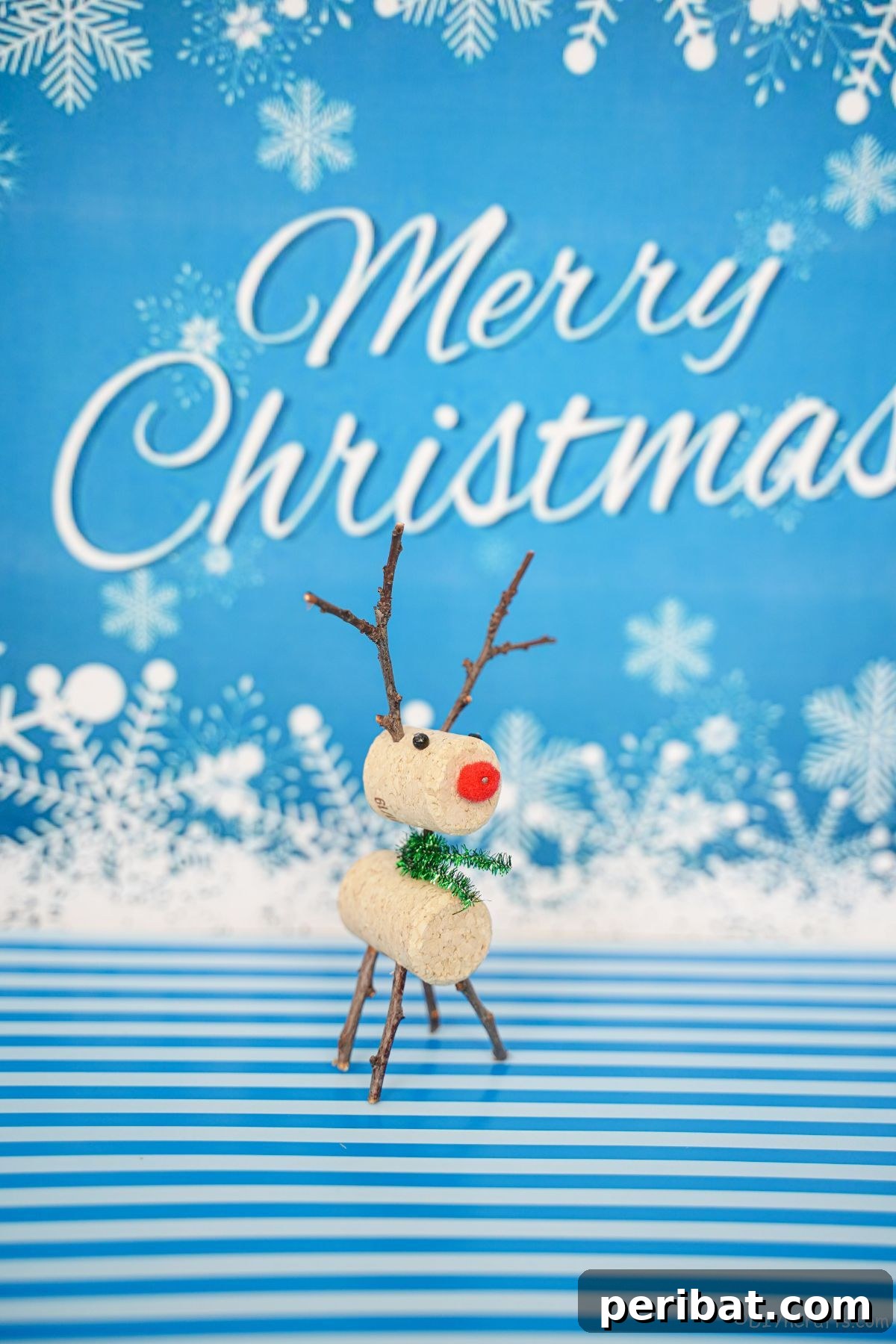 Whimsical Wine Cork Reindeer Ornament 2 Small wine cork reindeer standing on a blue and white patterned surface, with a blurred 'Merry Christmas' sign in the background, creating a festive holiday scene.