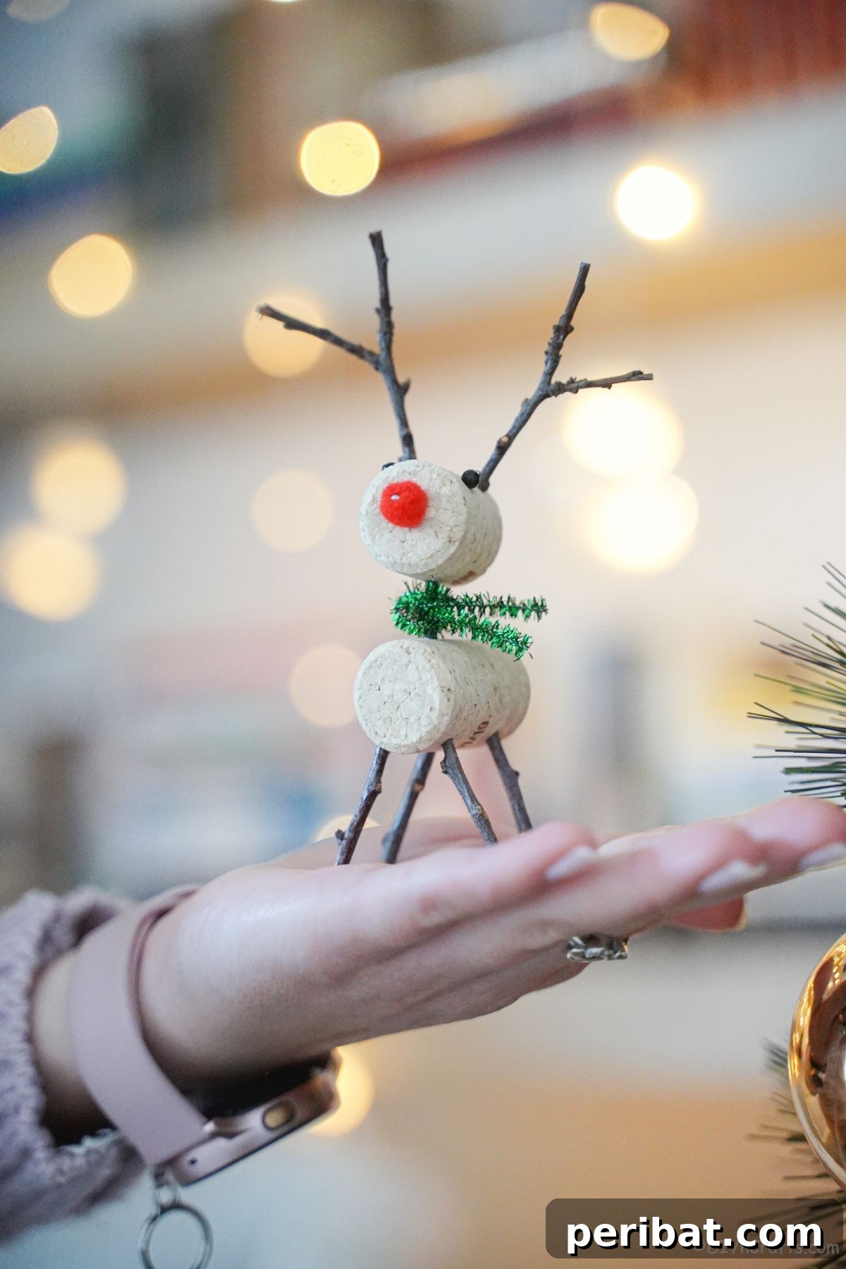 Whimsical Wine Cork Reindeer Ornament 9 A hand gently holding a finished wine cork reindeer, featuring a green pipe cleaner scarf, showcasing the completed DIY craft.