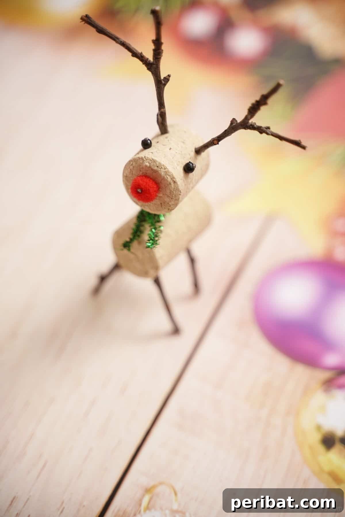 Whimsical Wine Cork Reindeer Ornament 4 A festive red-nosed wine cork reindeer, complete with delicate twig antlers, stands proudly on holiday-themed paper, embodying the spirit of Christmas.