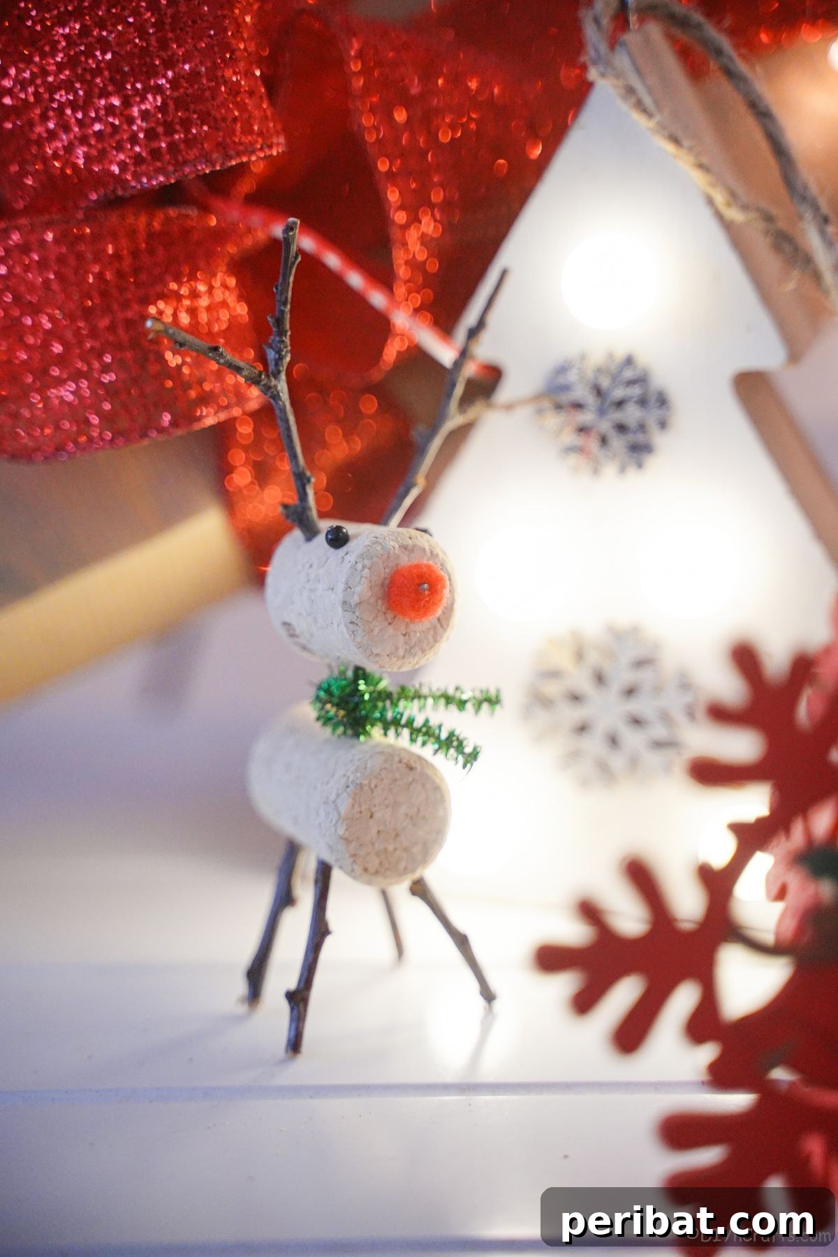 Whimsical Wine Cork Reindeer Ornament 6 A charming cork reindeer stands proudly in front of a white mini Christmas tree adorned with red snowflake ornaments, creating a festive holiday display.