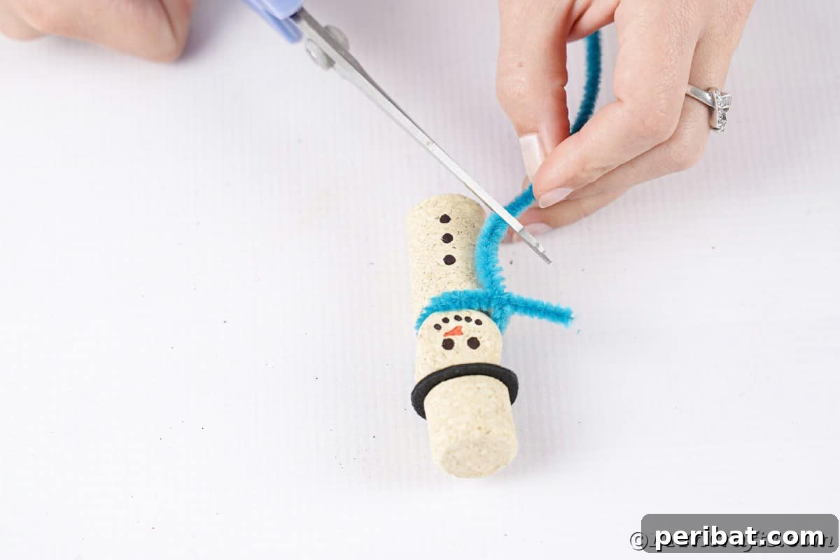 hand trimming blue pipe cleaner off bottom of wine cork snowman