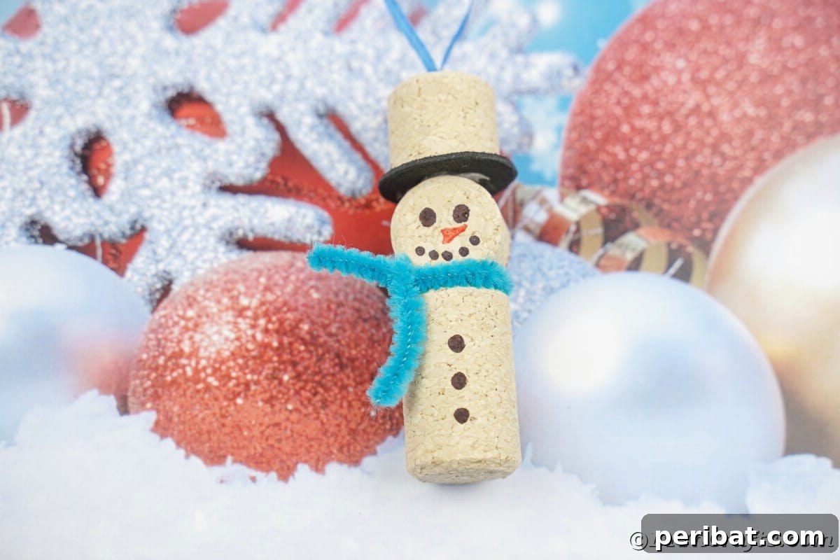 wine cork snowman ornament with blue pipe cleaner scarf on fake ornament paper