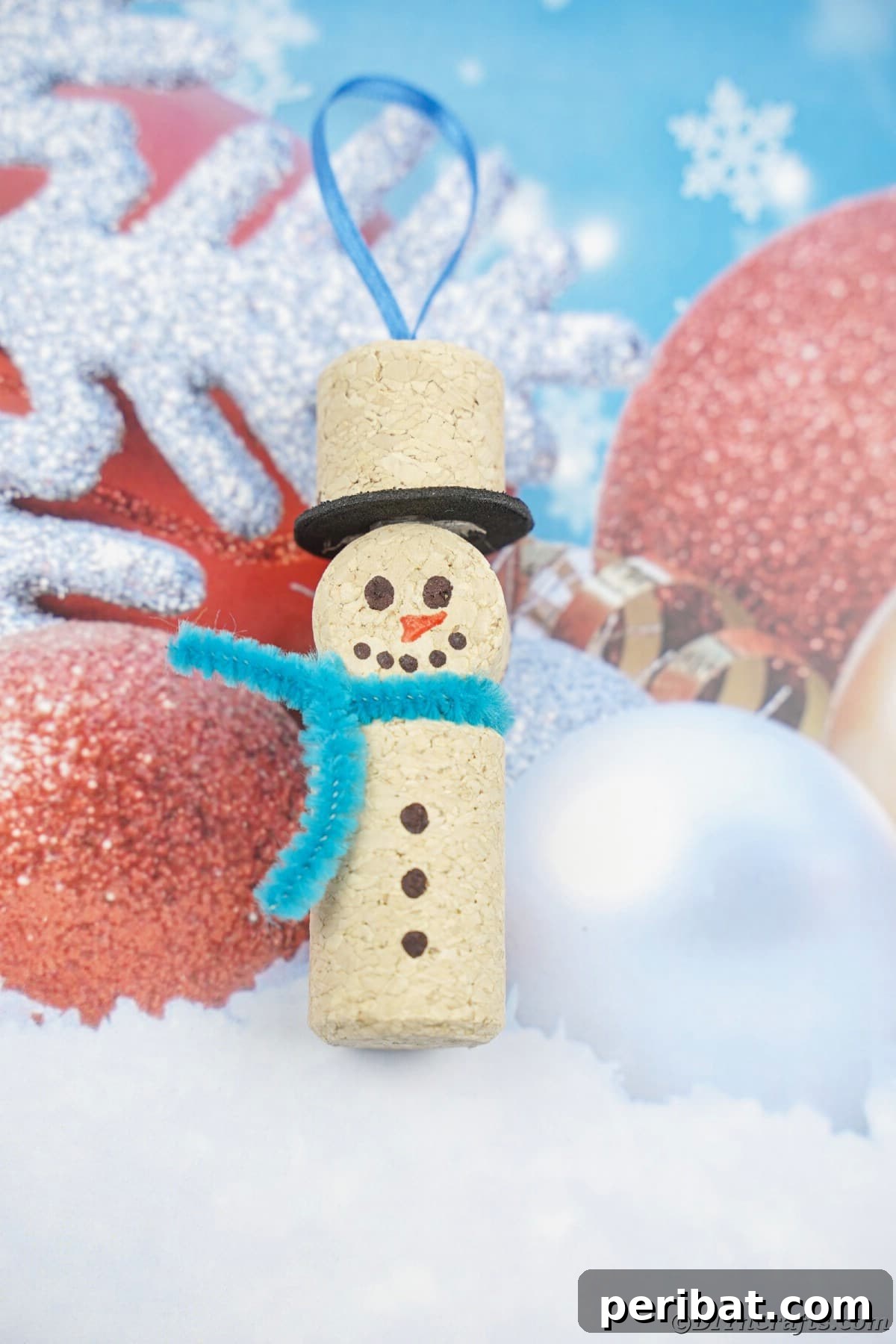 snowman ornament made of cork with blue pipe cleaner scarf on blue and white paper
