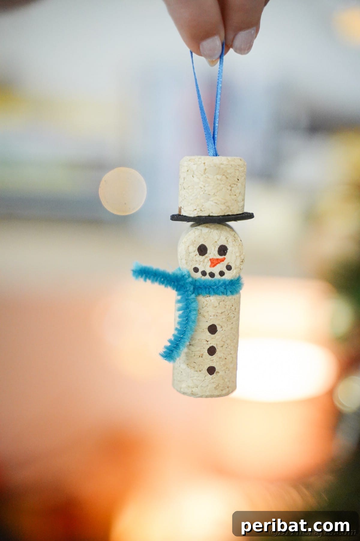 cork snowman with blue scarf being held in front of twinkling lights