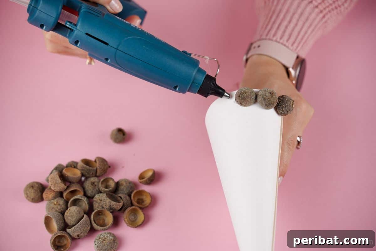 hand holding cone and gluing acorns on bottom
