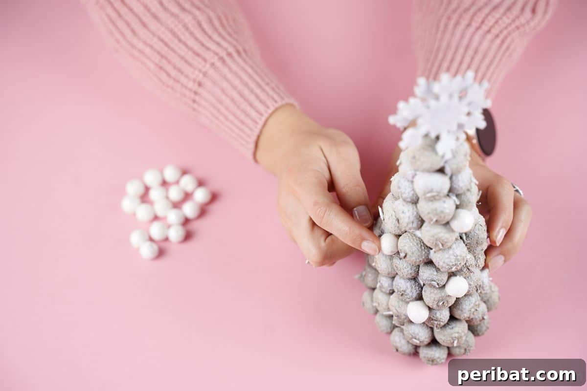 hand gluing white pom poms onto acorn cap tree