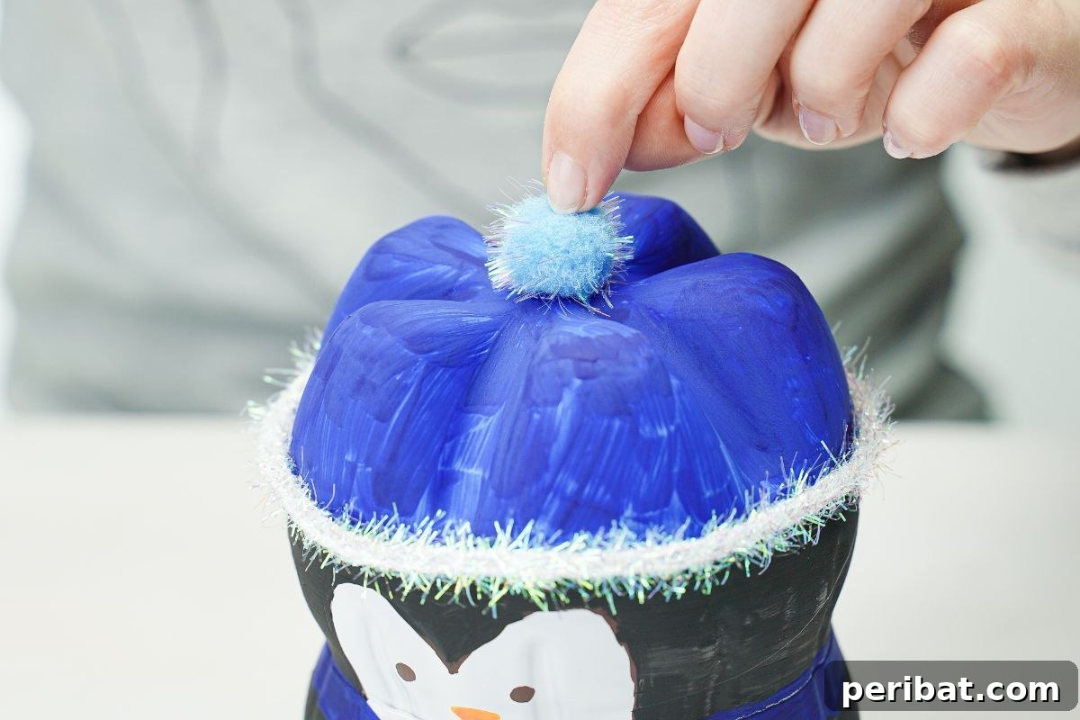 Upcycled Plastic Bottle Penguin Craft for Kids 20 hand holding blue pom pom on top of bottle