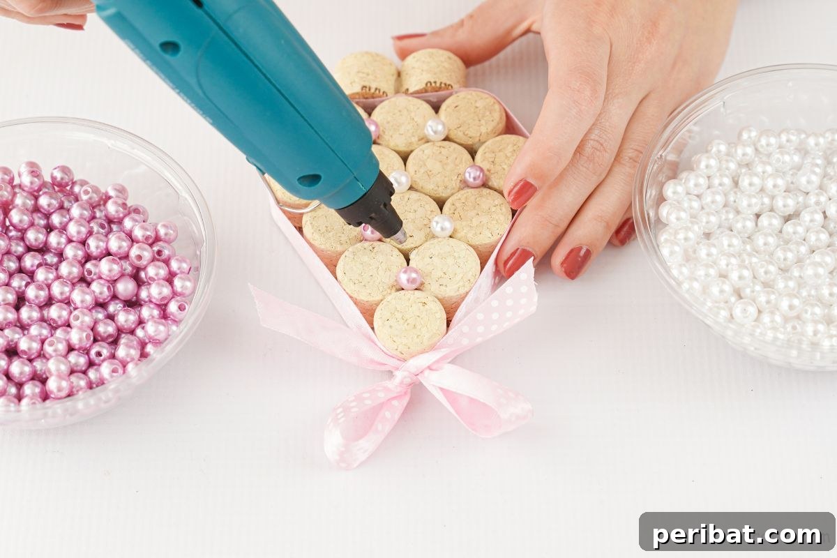glue gun gluing beads on cork tree, adding mini decorations to the handmade Christmas tree