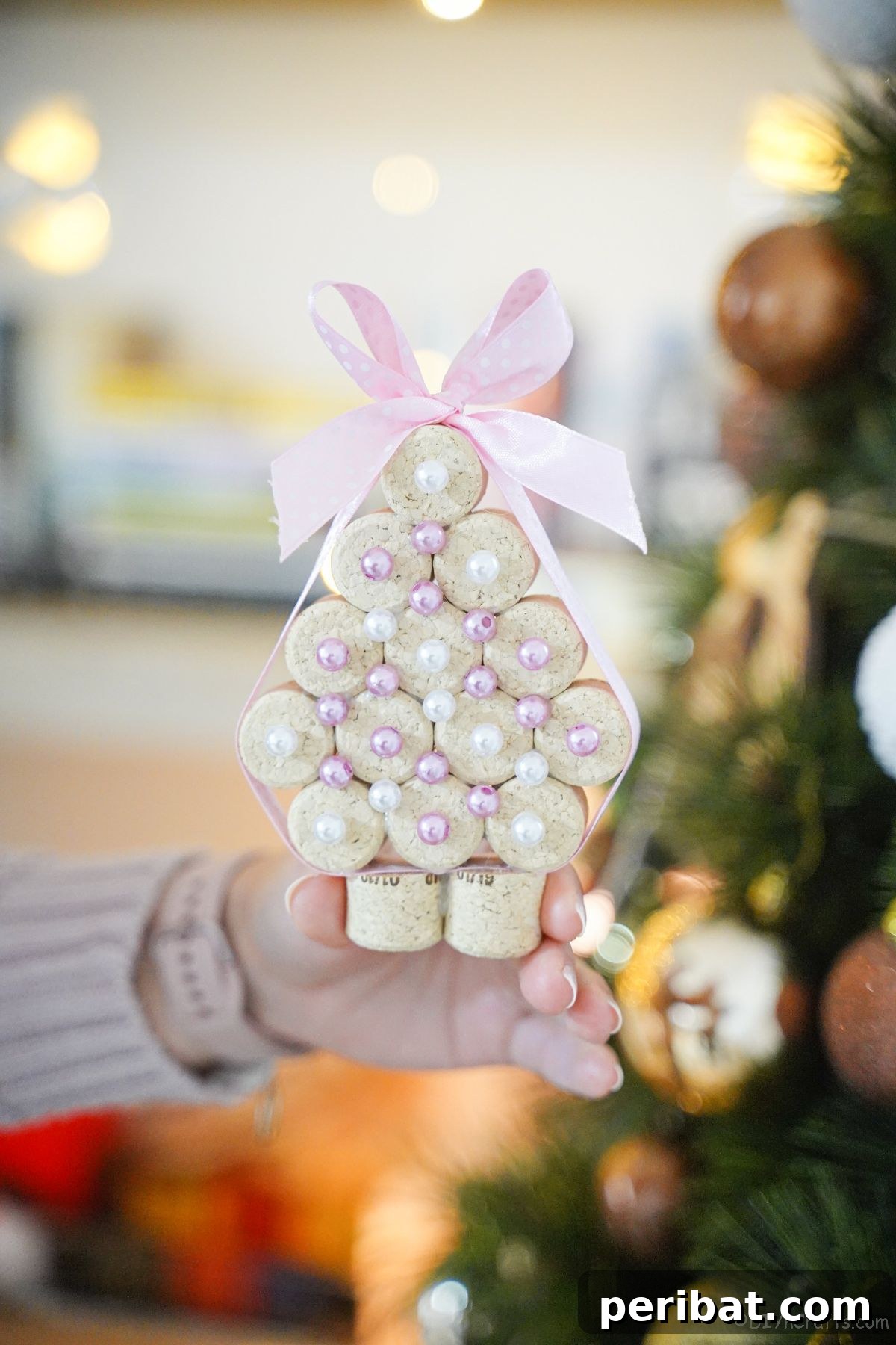 lady in sweater holding cork miniature tree in front of holiday tree, proudly showcasing DIY decor