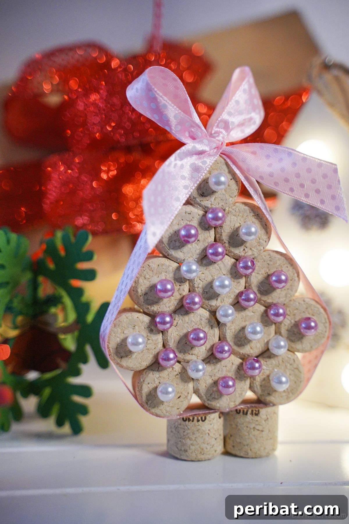 cork mini tree with pink and white beads on white table with red flower in background, a cheerful handmade decoration